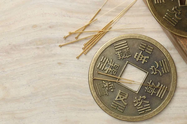 Acupuncture needles and ancient coin on beige marble table, flat lay. Space for text