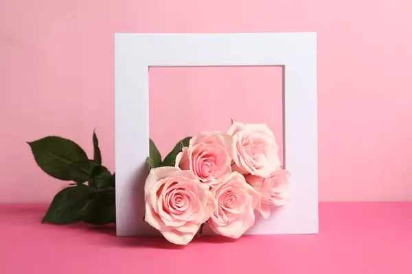 White frame and beautiful roses on pink table