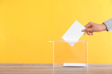 Oy sandığına oy veren kadın, tahta masada turuncu arka planda, yakın planda.