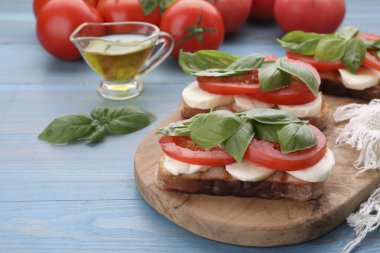 Mozarella, domates ve açık mavi ahşap masada fesleğenli lezzetli Caprese sandviçleri. Metin için boşluk