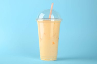 Açık mavi arka planda plastik bir bardak lezzetli smoothie.