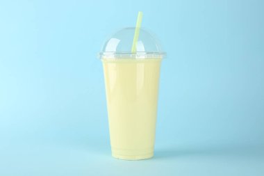 Açık mavi arka planda plastik bir bardak lezzetli smoothie.