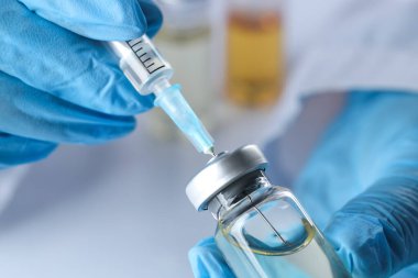 Şırıngayı cam şişeden alınan ilaçlarla dolduran doktor.
