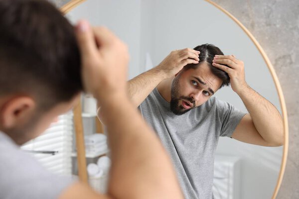 Человек с перхоти в темных волосах возле зеркала в ванной комнате