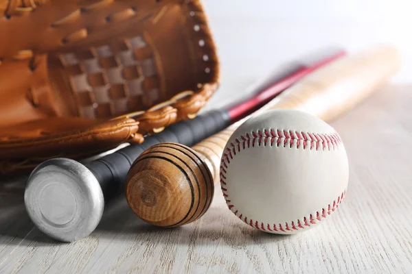 Baseball glove, bats and ball on white wooden table, closeup