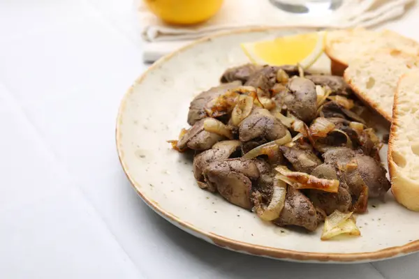 Tasty fried chicken liver with onion served on white tiled table, closeup. Space for text