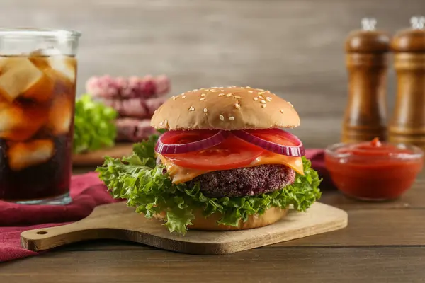 Tasty vegetarian burger with beet patty, sauce and soda drink on wooden table