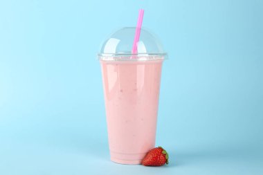 Plastik bardak lezzetli smoothie ve açık mavi arka planda taze çilek.