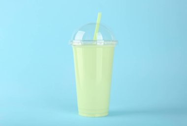 Açık mavi arka planda plastik bir bardak lezzetli smoothie.