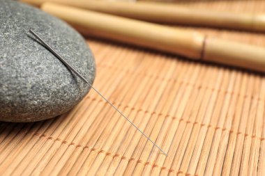 Bambu hasırının üzerinde akupunktur iğnesi ve spa taşı, yakın plan. Metin için boşluk