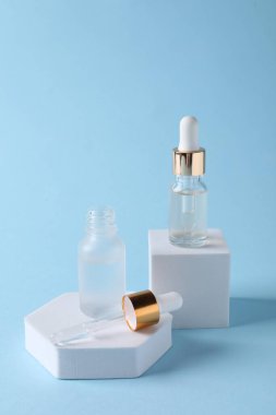 Açık mavi arka planda kozmetik serumlu şişelerin sunumu