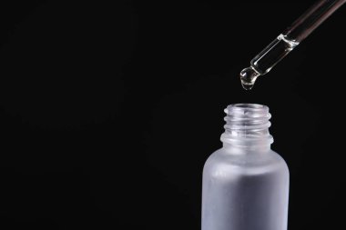 Siyah arka planda pipetten şişeye kozmetik serumu damlatılıyor, metin için boşluk