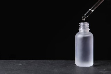Pipetten şişeye kozmetik serumu damlatıyor. Gri masa üzerinde, mesaj için yer var.