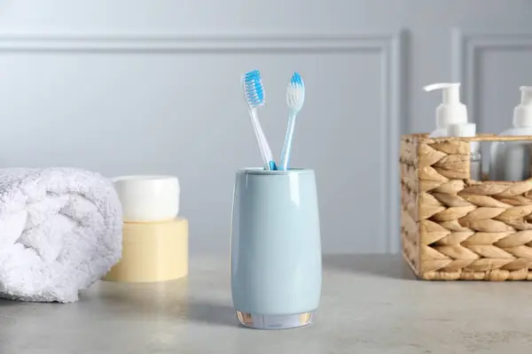 Plastic toothbrushes in holder, towel and cosmetic products on light grey table