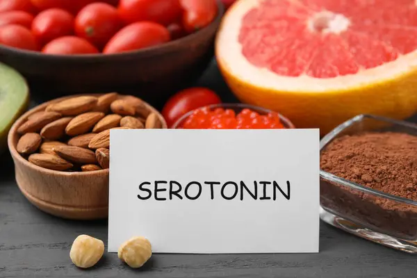 Many different products and card with word Serotonin on grey wooden table, closeup. Natural antidepressants