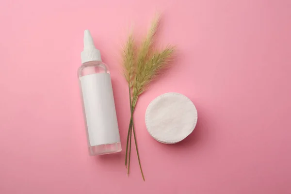 Bottle of makeup remover, cotton pads and spikelets on pink background, flat lay