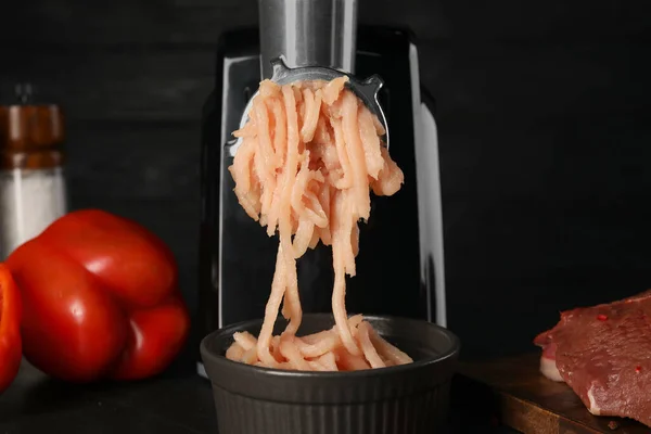 Electric meat grinder with chicken mince and products on black table, closeup