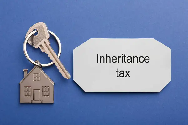 Inheritance Tax. Card and key with key chain in shape of house on blue background, top view