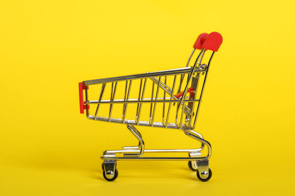 Small metal shopping cart on yellow background