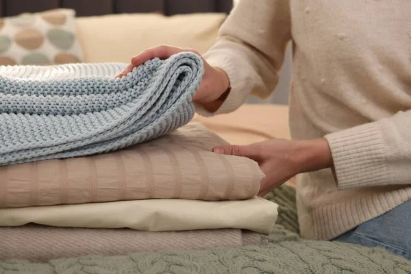 Woman with stack of different folded blankets on bed, closeup. Home textile
