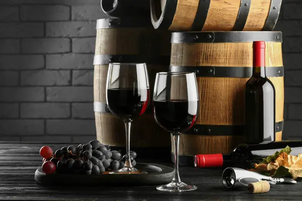Delicious wine, wooden barrels and fresh grapes on black table