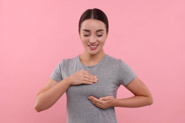 Güzel genç bir kadın pembe arka planda göğüs muayenesi yapıyor.