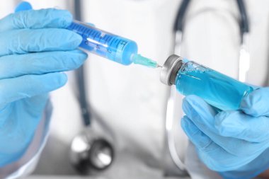 Şırıngayı cam şişeden alınan ilaçlarla dolduran doktor.