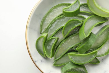 Bir kase taze aloe vera dilimleri beyaz masada, en üstte.