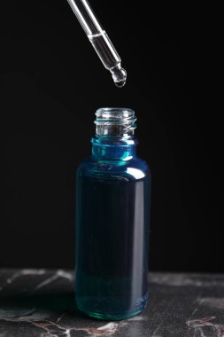 Gri mermer masada pipetten şişeye kozmetik serumu damlatıyor.