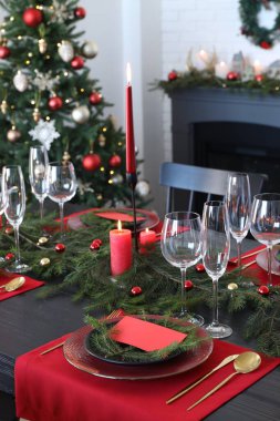 Şenlikli bir odada bulaşık takımı ve yanan mumlarla şık bir Noel sofrası.