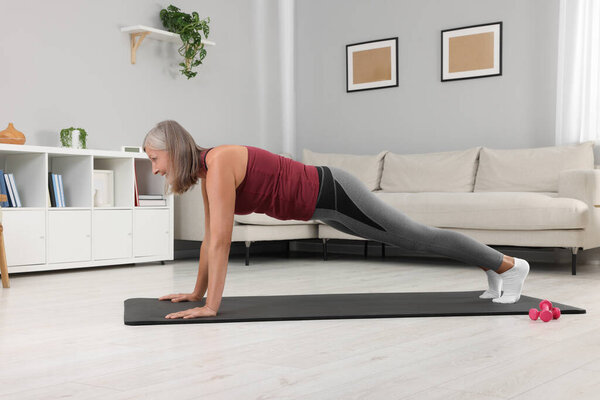 Senior woman in sportswear doing exercises on fitness mat at home