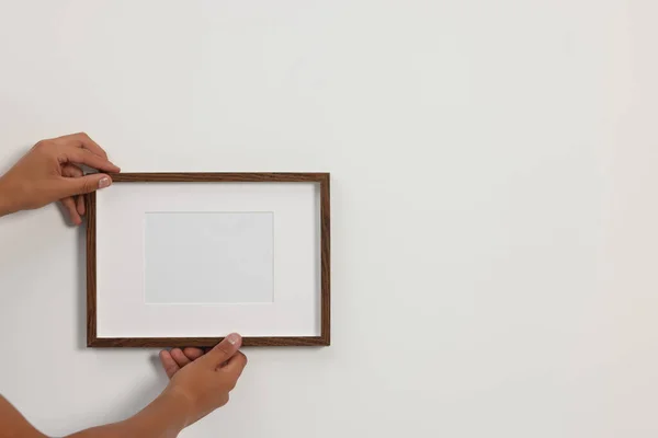 Young man hanging picture frame on white wall indoors, closeup