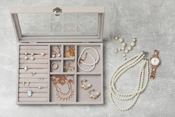 Jewelry box with many different accessories on light grey table, flat lay