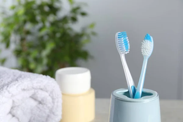 Plastic toothbrushes in holder, towel and cosmetic product on table, closeup