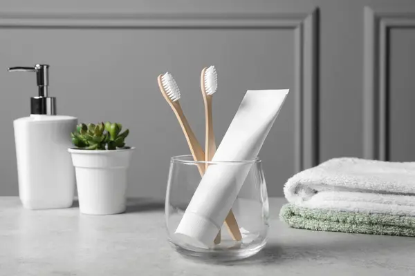 Bamboo toothbrushes in holder, toothpaste, houseplant and towels on light grey table