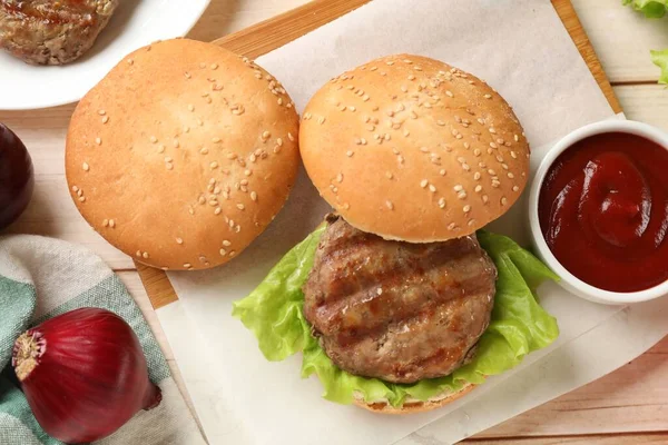 Delicious fried patty, lettuce, buns and sauce on wooden table, flat lay. Making hamburger