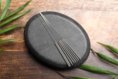 Akupunktur iğneleri, spa taşı ve yaprak ahşap masa, düz yatar