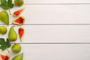 Beyaz ahşap masa üzerinde yaprakları olan yeşil incirler ve düz bir döşeme. Metin için boşluk