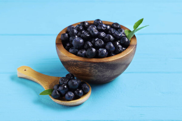 Ripe bilberries and leaves on light blue wooden table, closeup