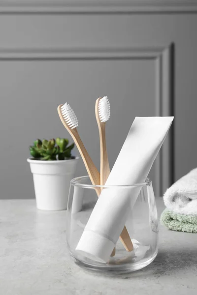 Bamboo toothbrushes in holder, toothpaste, houseplant and towels on light grey table