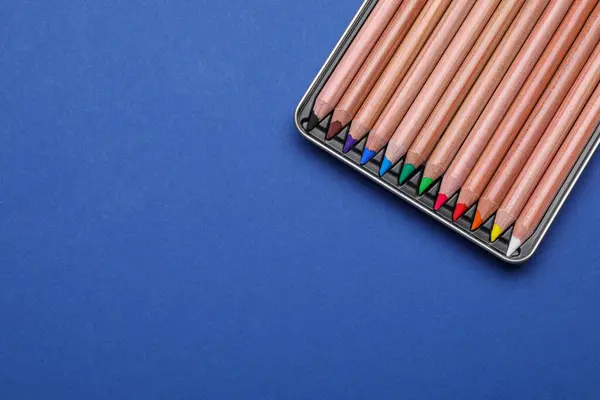 Colorful pastel pencils in box on blue background, top view with space for text. Drawing supplies