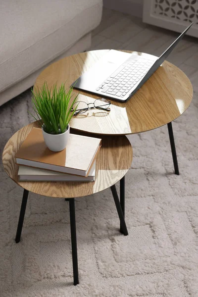 Potted artificial plant, laptop and books on wooden nesting tables indoors, above view