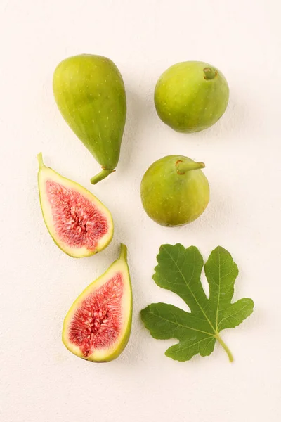 Cut and whole green figs with leaf on light table, flat lay