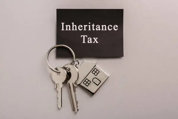 Card with phrase Inheritance Tax and keys with house shaped key chain on grey background, top view