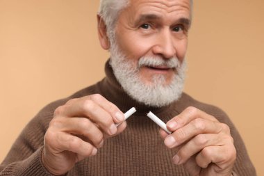 Stop smoking concept. Senior man holding pieces of broken cigarette on beige background, selective focus clipart