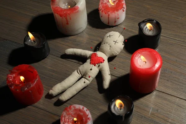 Voodoo doll with pins in circle of burning candles on wooden table