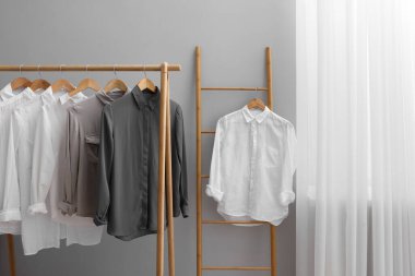 Odadaki gri duvarın yanında merdivenlerde ve askılarda asılı farklı şık gömlekler. Giysileri düzenleme