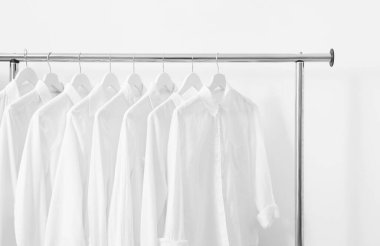 Beyaz duvarın yanında farklı şık gömlekler var. Giysileri düzenleme