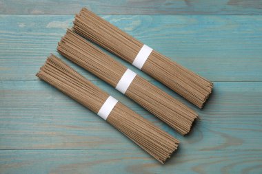 Açık mavi ahşap masa üzerinde pişmemiş karabuğday eriştesi (soba), düz yatıyordu