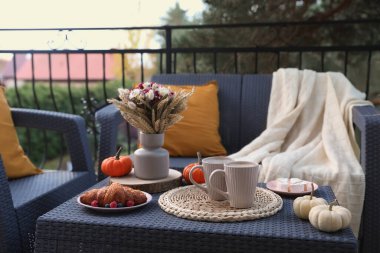 Terasta rattan mobilyalarla dinlen. İç, tatlı ve sonbahar dekoru masada.